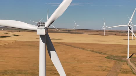 a drone flies across a prairie farmland wind farm and past a giant windmill in southern alberta, canada