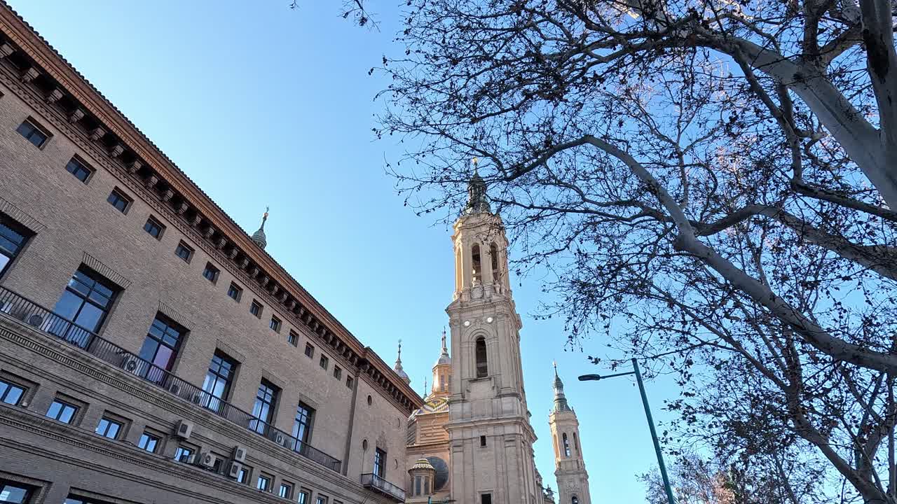 Baroque-style Basílica del Pilar in Zaragoza, Spain, seen through bare winter branches and surrounded by urban architecture