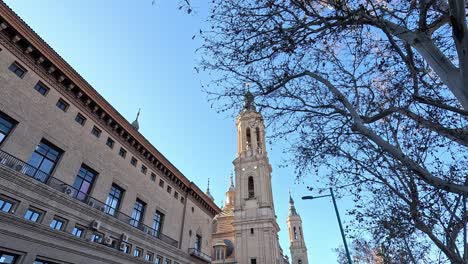 baroque-style basílica del pilar in zaragoza, spain, seen through bare winter branches and surrounded by urban architecture