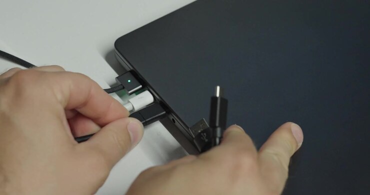 Persona che cerca di collegare un altro dispositivo USB a un laptop con tutte le porte già occupate, illustrando connettività limitata e porte USB insufficienti