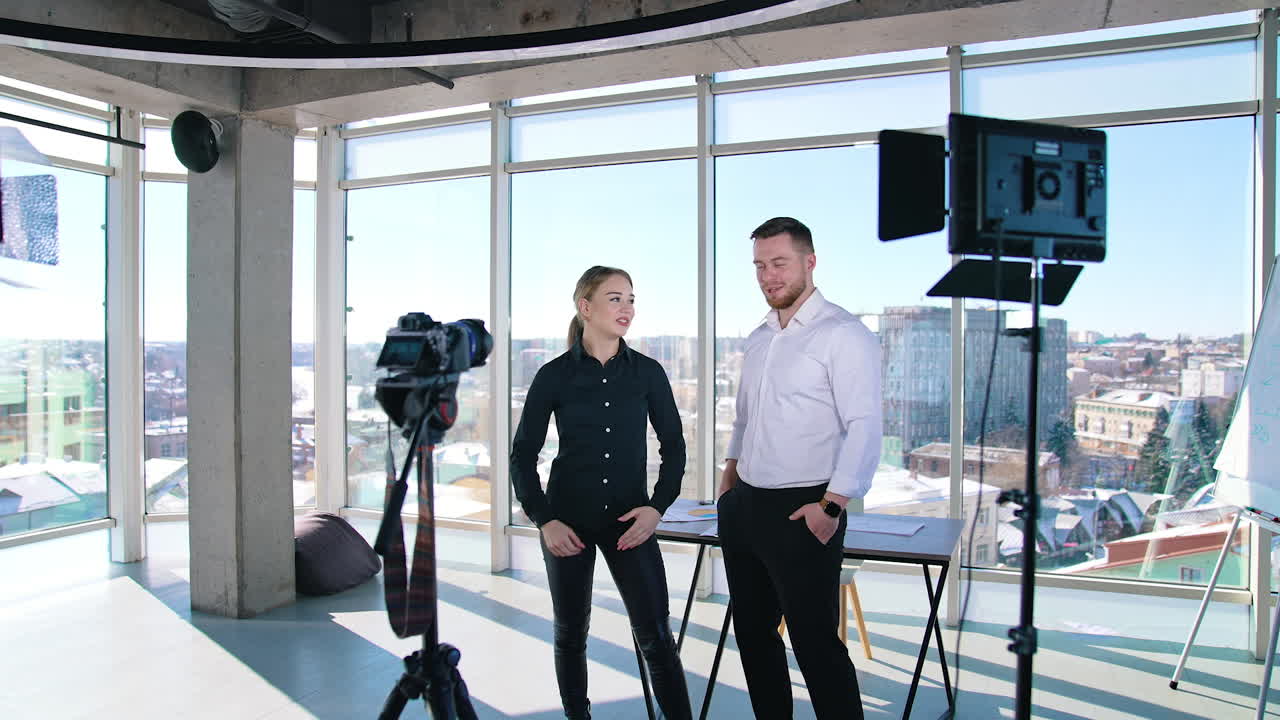 Young woman recording video in front of camera. Business people standing in office center and talking about projects on camera on large windows background