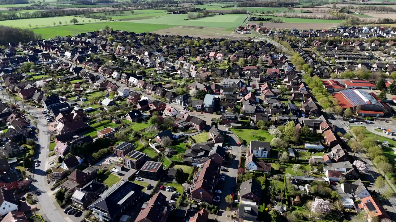 Peaceful and charming american neighborhood with single family houses and rural farm fields in background. Aerial forward wide shot. Sunny day in spring season. Beautiful cityscape landscape.