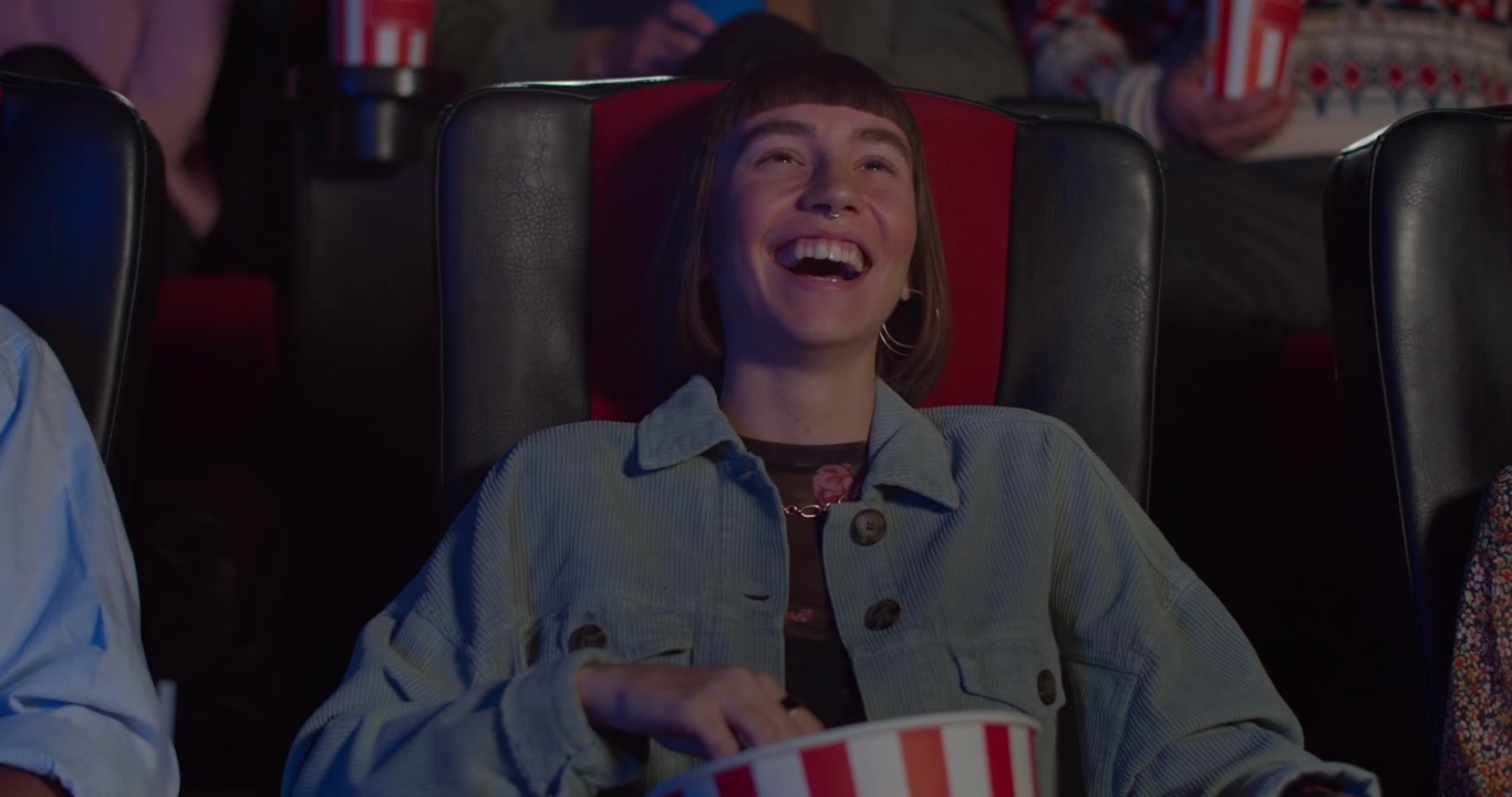 Ung kvinde griner, mens hun ser en film i en biograf