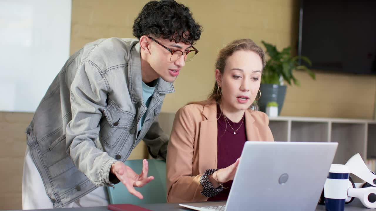 Diverse coworkers gesturing and guiding woman typing and pointing at laptop screen at desk