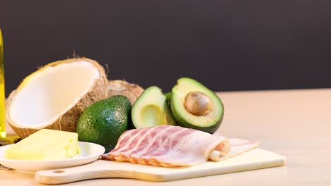 a variety of healthy fats including oils, nuts, and avocados are arranged on a wooden surface under bright lighting
