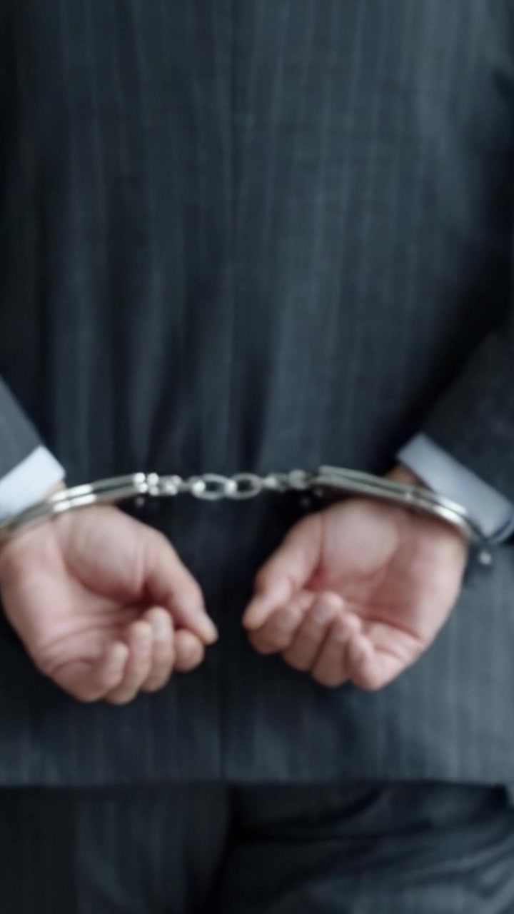 En skarp fremstilling af tilbageholdenhed og indespærring, der viser en person i jakkesæt bundet med håndjern, og illustrerer temaer om fangenskab, lov og retfærdighed i et bymiljø.