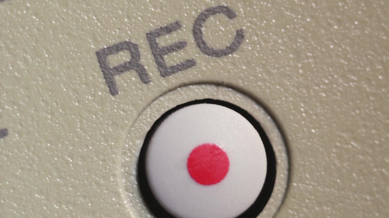 Angled macro shot of finger pressing white record button with red dot on beige controller