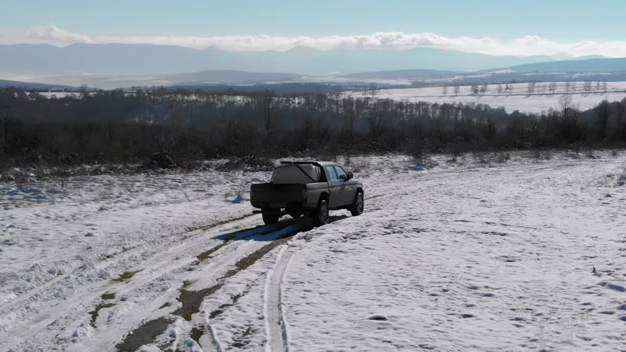 Pickup-bil med last på åpent lasteplan kjører på snødekt vei i Bulgaria om vinteren - sporing droneopptak