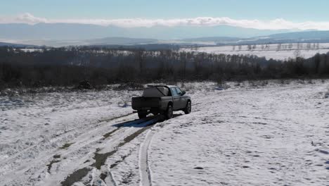 pickup truck with load in open cargo area driving on snowy road in bulgaria during winter - tracking drone shot