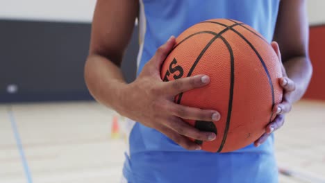 Portrait-of-african-american-male-basketball-player-holding-ball-in-indoor-court,-in-slow-motion