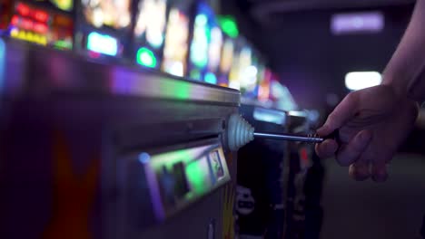 person dropping a coin into an arcade game pinball machine and pulling the spring back to shoot the ball