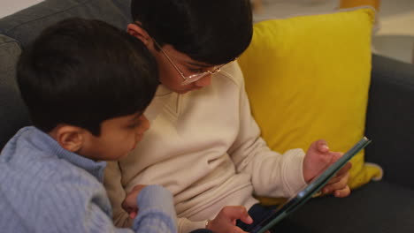 two young boys sitting on sofa at home playing games or streaming onto digital tablet 10