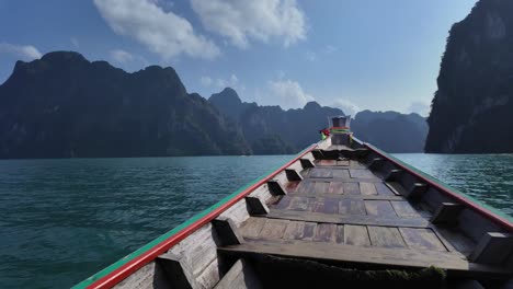 un barco tradicional de madera veloz navega sobre el agua entre las pintorescas montañas tropicales en el parque nacional khao sok de tailandia.