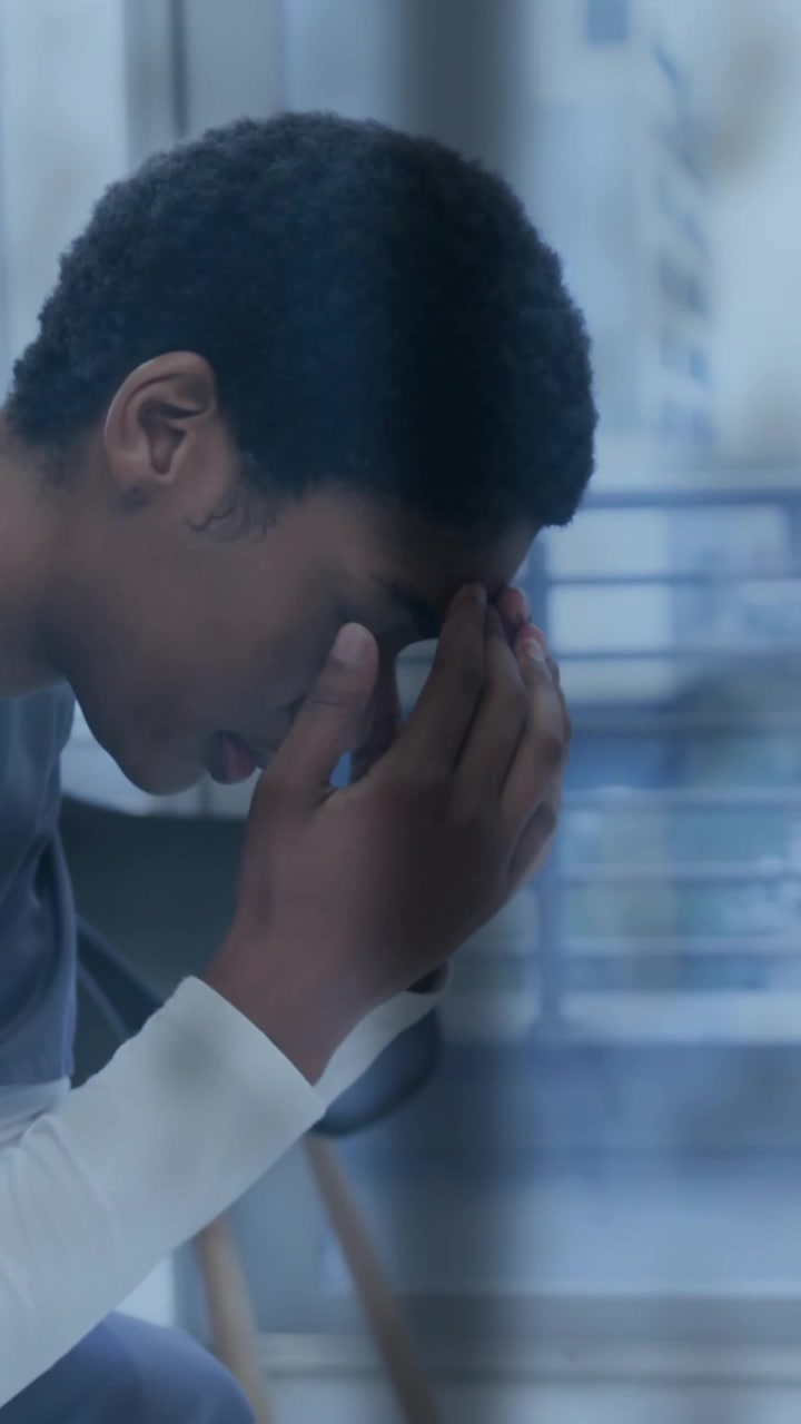Animation of rain on window over unhappy african american female doctor holding head in hands