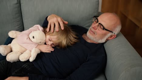 niña pequeña con juguete durmiendo en el pecho de su abuelo en la sala de estar