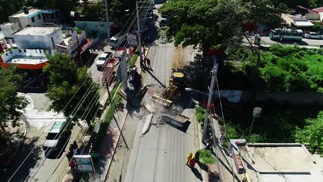 Aerial-view-of-a-machine-and-crew-repairing-hurricane-aftermath,-on-city-streets---descending,-drone-shot