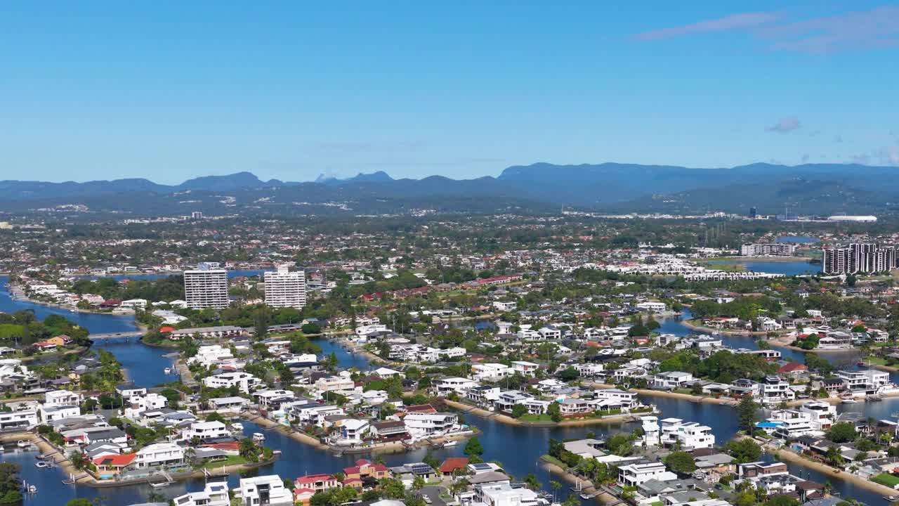 Panoramic aerial view of Gold Coast, Australia, showcasing urban landscape, waterways, and distant mountains under clear blue skies