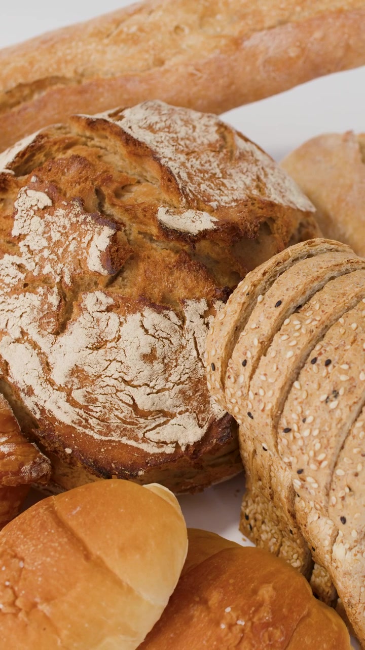 Slow camera pan across various artisanal breads, croissants, and baguettes under bright studio lighting.