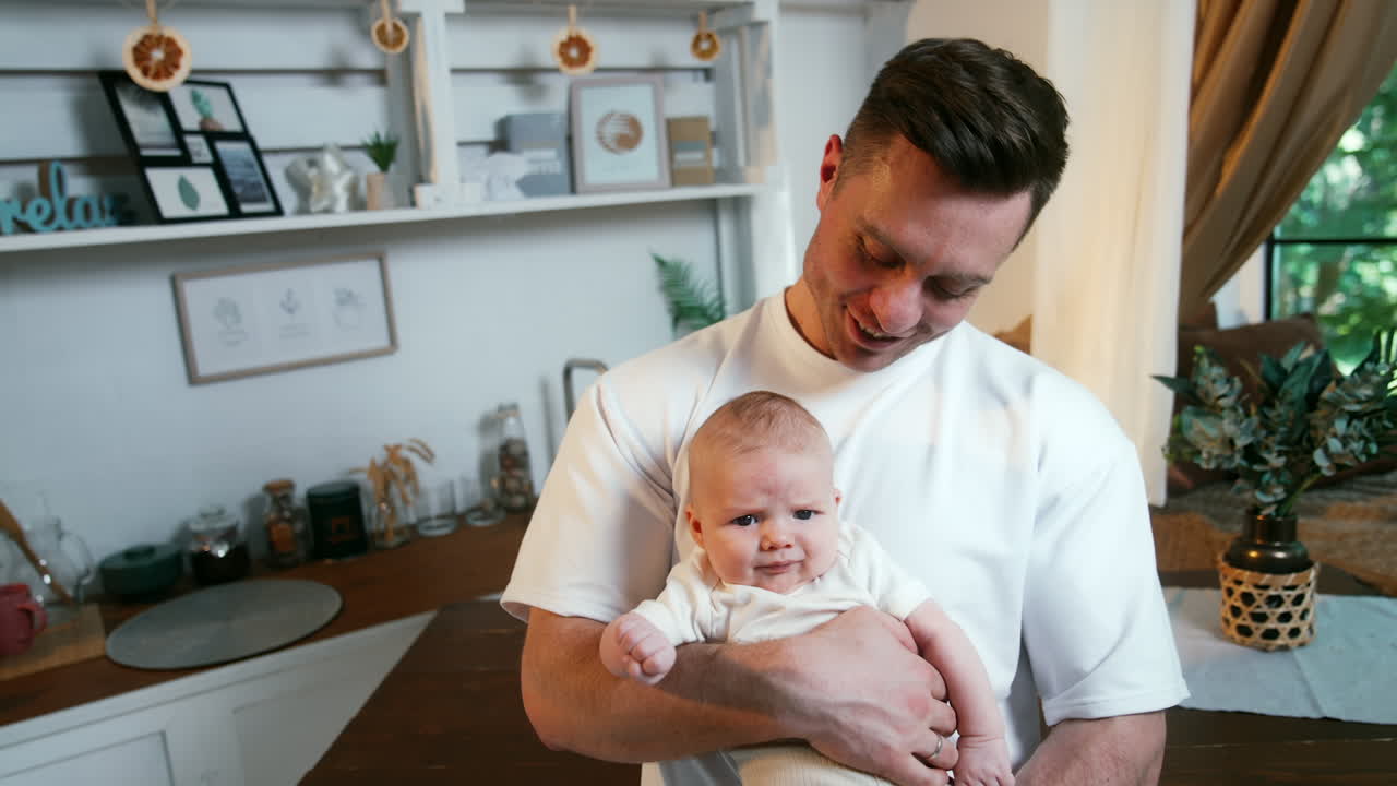Caucasian man wearing white t-shirt holding a tiny newborn in white t-shirt. Like father like son. Close up.