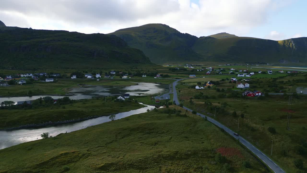 volando hacia las montañas cubiertas de hierba verde en el horizonte cruzando el océano y la estrecha carretera costera en lofoten, norte de noruega