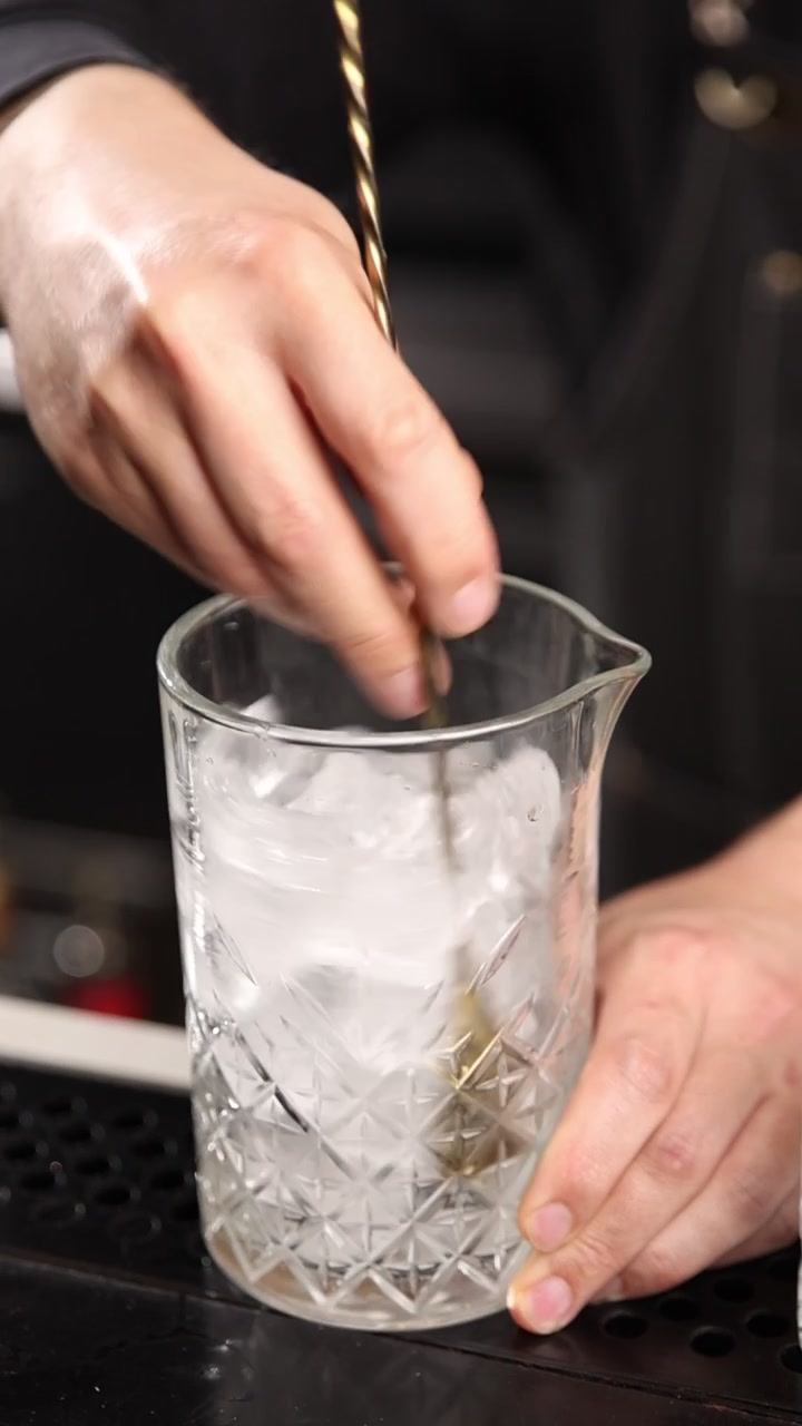Barman che mescola ghiaccio in un mixing glass con un bar spoon