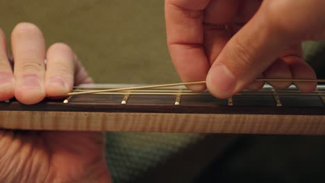 luthier tirando de las nuevas cuerdas para aflojarlas después de volver a encordar la guitarra acústica para evitar que se desafine
