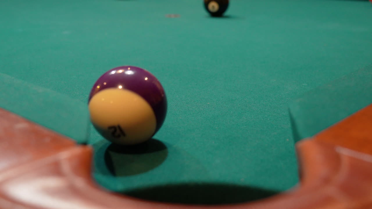 Pool Balls are Broken on an 8 Ball Triangle Rack and the Purple Stripe 12 Ball Slowly Rolls towards Edge of Corner Pocket, Closeup with Solids and Stripes Scattering Across the Table with Green Felt