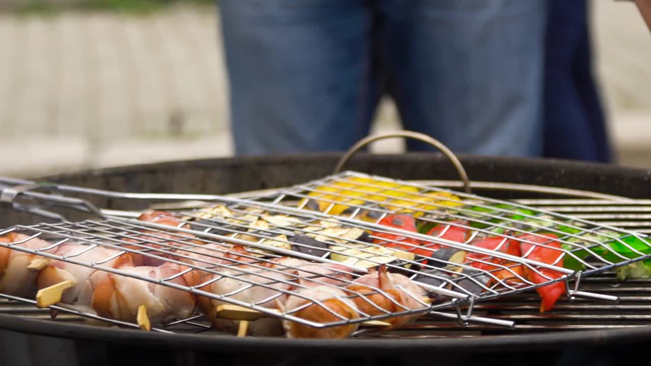야외 바베큐에서 그릴 채소와 베이컨으로 포장된 소시지를 먹습니다.