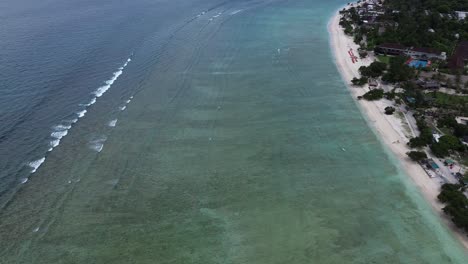 aerial view slowly panning right along the beach with clear shallow water and visible waves. sunny weather