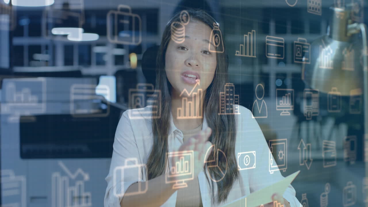 animación de íconos de negocios sobre mujer de negocios casual biracial haciendo una llamada de video en el escritorio de la oficina