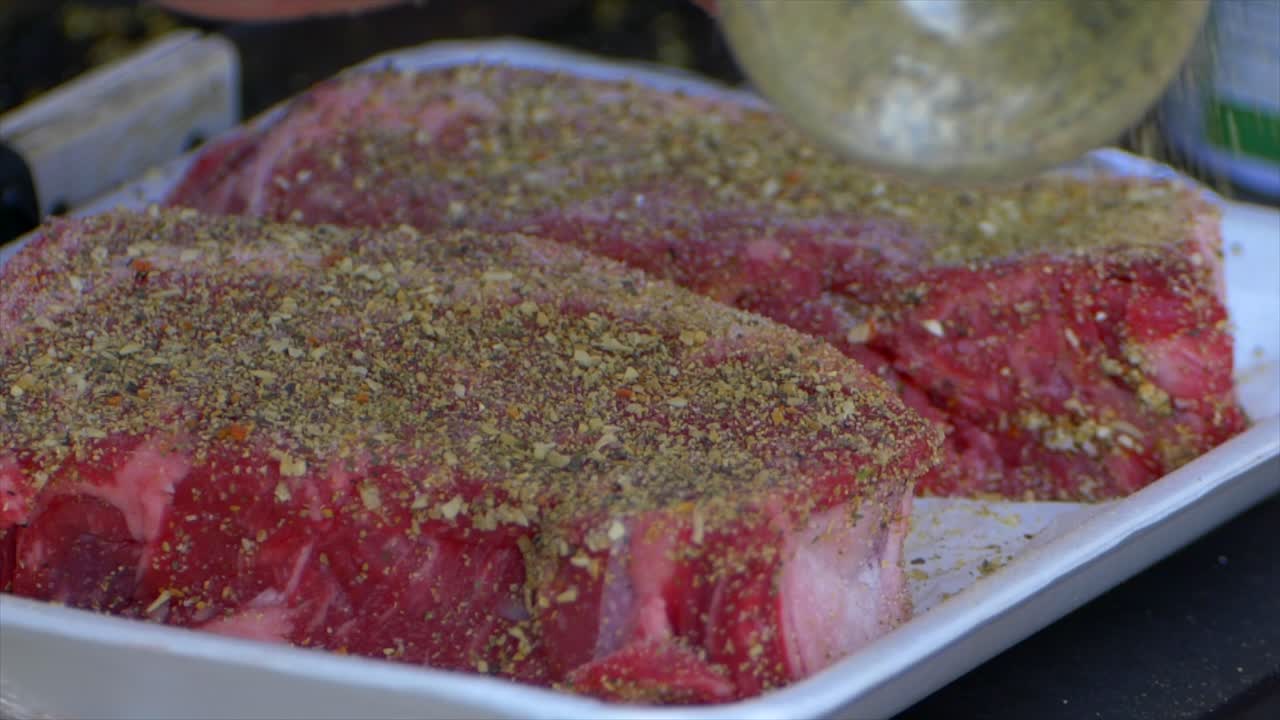 Una mano versa spezie su una bistecca di costata già condita, al rallentatore.