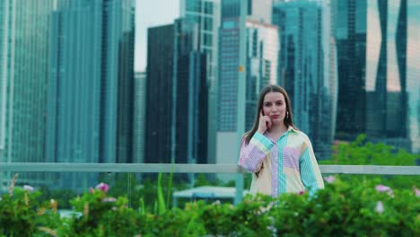 beautiful caucasian girl in a thinking position, daylight, outside in chicago with skyscrapers in background and green bushes in foregrround