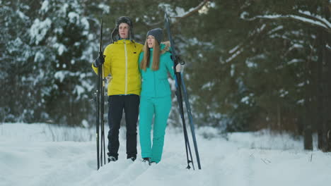 Side-view-portrait-of-active-young-couple-carrying-skis-chatting-on-the-way-back-in-beautiful-winter-forest,-copy-space