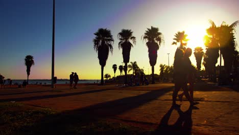 Silueta-De-Personas-Caminando-En-El-Paseo-Marítimo-Al-Lado-Del-Océano-Durante-La-Puesta-De-Sol-En-Brasilia,-Brasil