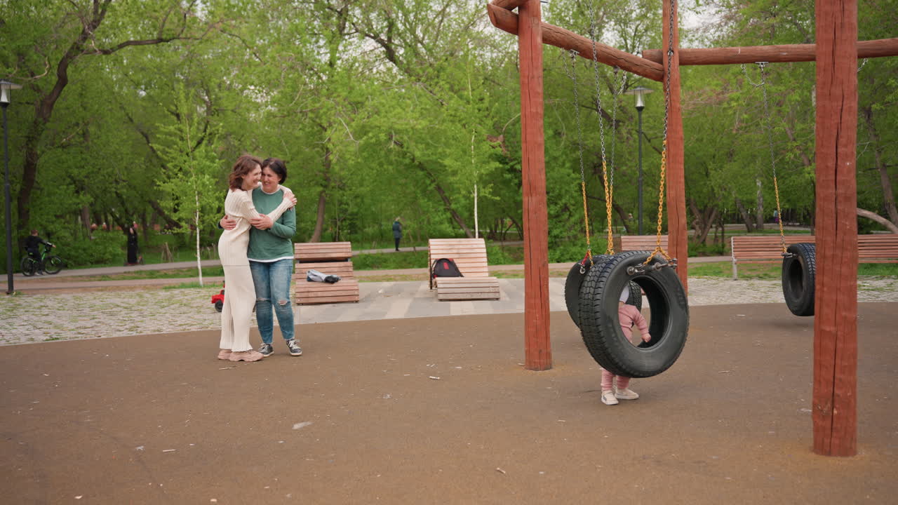 Couple Hugging At Playground Tire Swing, Soft Afternoon Light And Leafy Trees, Wooden Swing Frame With Hanging Tire, Two Adults In Casual Clothing Embrace Beside Empty Bench, Intimate Candid Moment