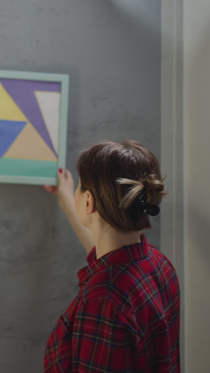 Woman seeks place for watercolor painting on grange style wall in restored living room. Interior designer works upon apartment decor. Home ornate trends