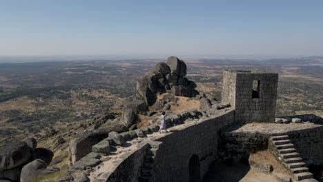 Einzigartige-Luftaufnahme-Vom-Schloss-Monsanto-In-Portugal-Und-Touristenfrau,-Die-Auf-Mauern-Läuft