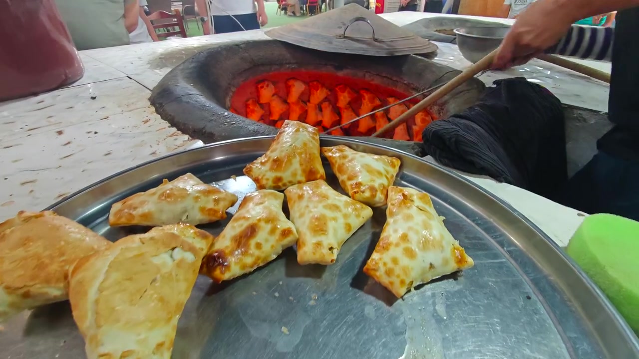 Fornaio che rimuove samsa appena sfornati da un tradizionale forno tandoor