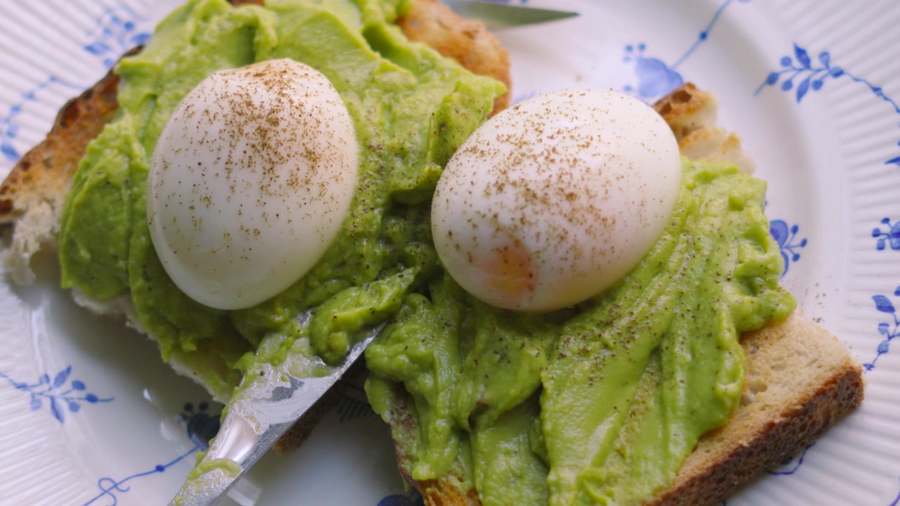 Vue de dessus d'œufs mollets frais avec de l'avocat écrasé sur du pain au levain. Petit-déjeuner sain et faible en gras.