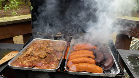 grilling delicious meat sausages and steaks on smoky grill with flames on foil trays