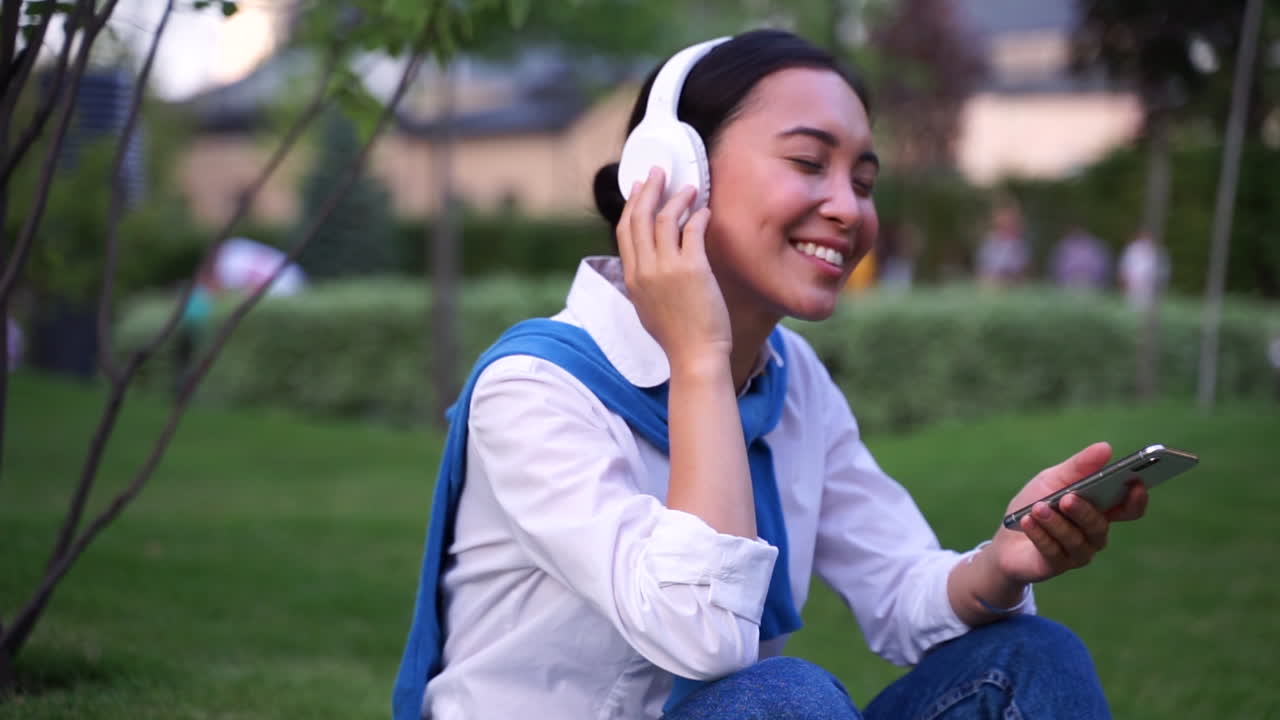 mujer alegre escuchando música con auriculares y teléfono al aire libre