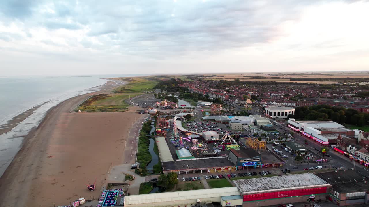 High above, video footage offers a view of the captivating sunset scene over Skegness, a quaint coastal town in the UK, with the town, promenade, pier, and coastline in the shot