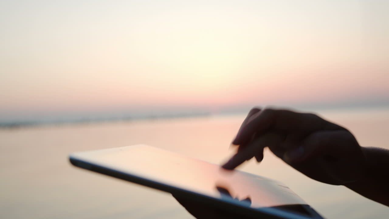 manos femeninas escribiendo en la tableta por el mar al atardecer