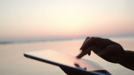 Weibliche-Hände-Tippen-Auf-Einem-Tablet-PC-Am-Meer-Bei-Sonnenuntergang