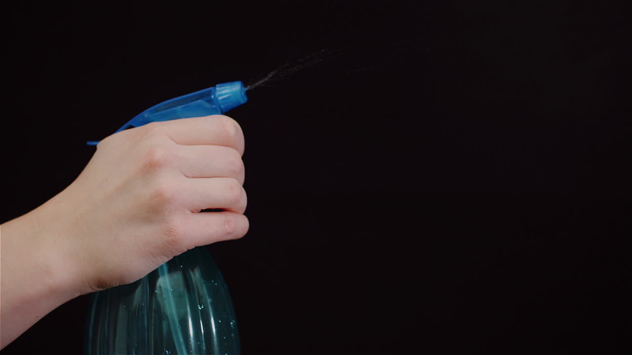 primer plano de la mano usando rociadores y rociando agua sobre fondo negro