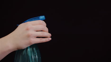 Close-Up-Of-Hand-Using-Sprinkler-And-Spraying-Water-On-Black-Background