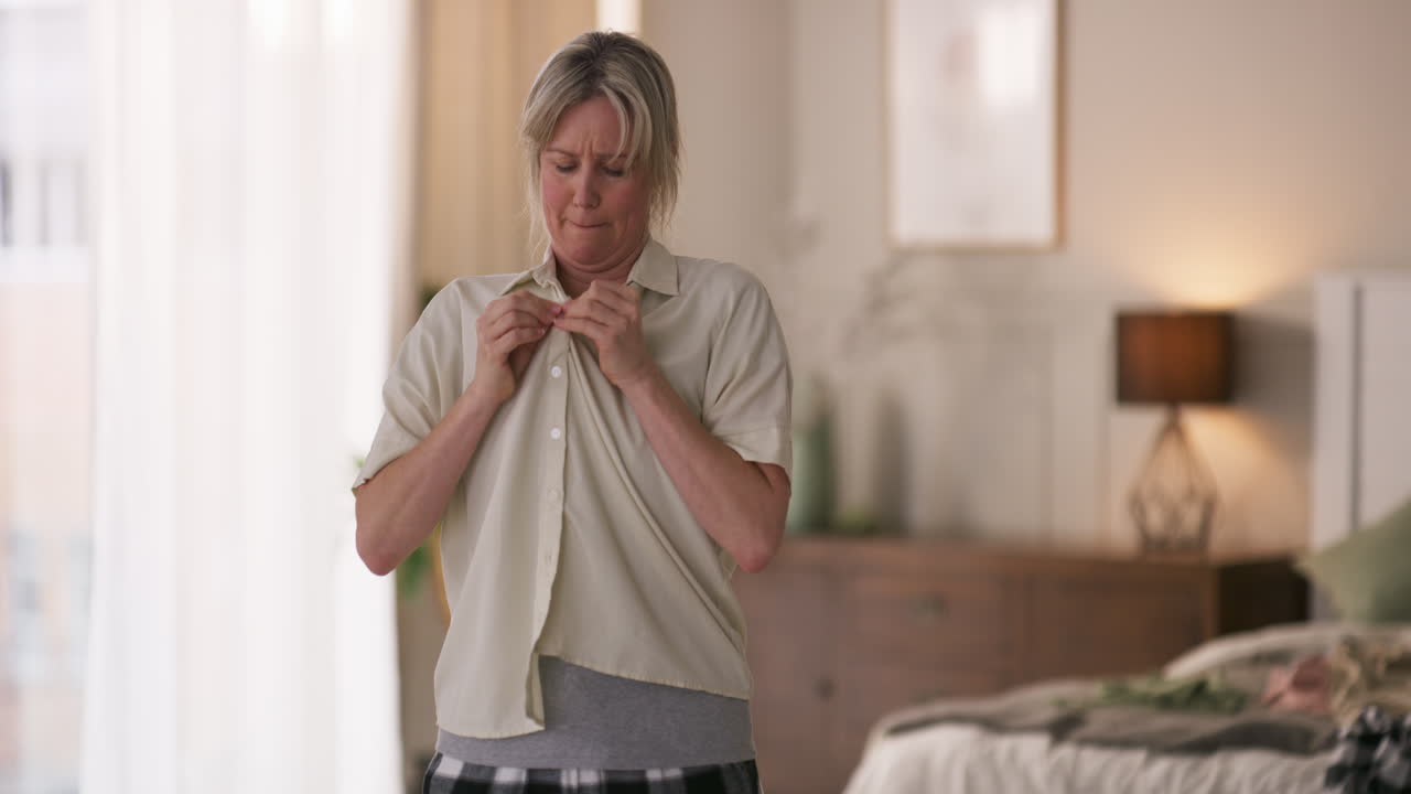 Woman buttoning shirt in bedroom