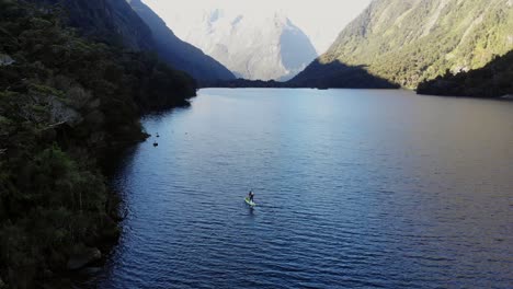 Paddle-boarder-on-remote-mountain-lake-surrounded-by-thick-rainforest-in-Fiordland-National-Park-in-New-Zealand