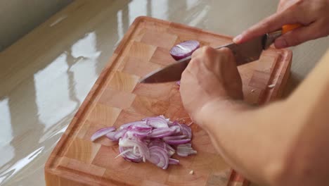 person's hand slicing red onion on wooden chopping board. - closeup shot