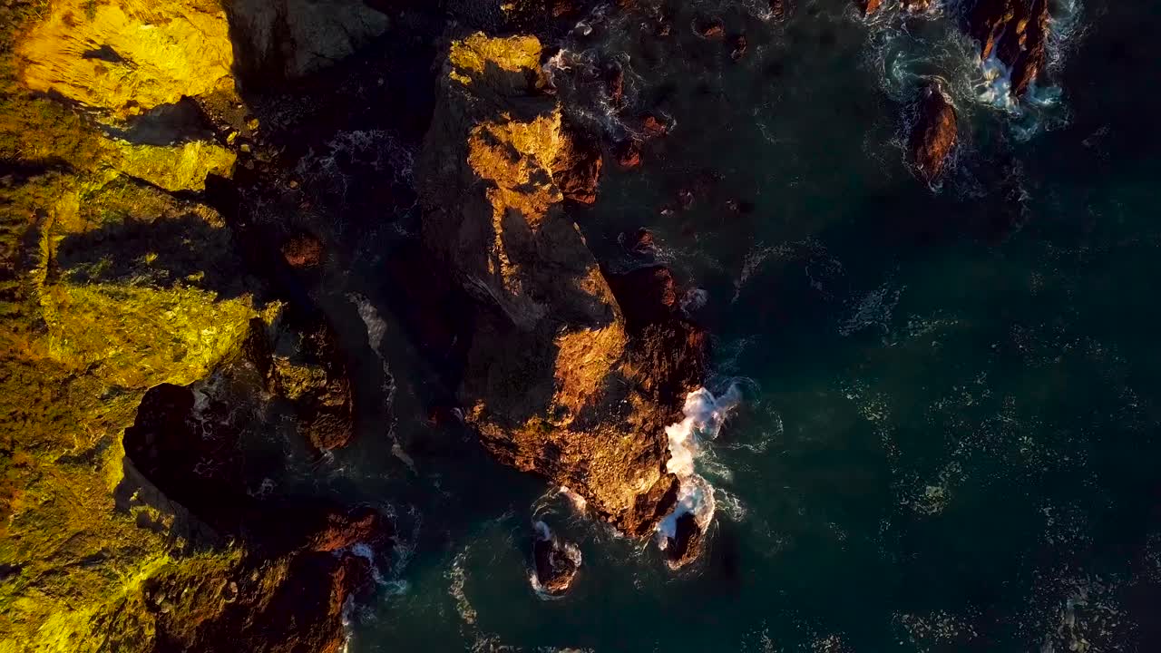 L'ultima luce del giorno illumina un'onda blu dell'oceano che si infrange contro le scogliere rocciose a Big Sur, California.